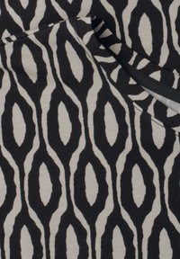 Tissu noir et beige avec un motif ovale allongé et audacieux et des coutures visibles le long d’un bord plié.