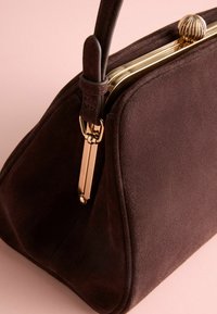 Geantă din suede maro cu o formă structurală, închidere cu clemă de culoare auriu, mâner scurt din piele și textură netedă.