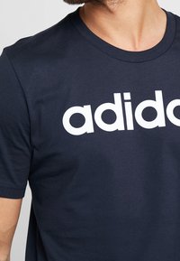 Camiseta de algodón de color azul marino con un gran logo blanco de "adidas" en el frente, con un clásico cuello redondo y mangas cortas.