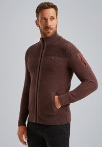 Brązowy sweter z dzianiny zapinany na zamek błyskawiczny, z wysokim ko�łnierzem, textured pattern, dwiema przednimi kieszeniami i naszywką na lewym rękawie.