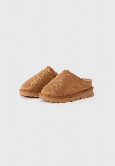 Tan slip-on träskor med en texturerad tygöverdel som har ett subtilt geometriskt mönster. Mjuk pälsfoder och en stabil, räfflad sula.