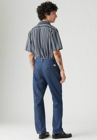 Tummansinisenä suorat farkut. Lyhythihainen raitapaita, jossa napitettava kaulus. Mustat rento kengät.