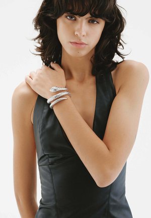 Pulsera en forma de serpiente plateada que se envuelve alrededor de la muñeca, con un diseño texturizado y escamas suaves, situada sobre una blusa de cuero negra.