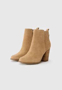 Bottines en daim beige clair, avec un bout effilé, un talon empilé texturé et une fermeture éclair sur le côté. Fini lisse avec une texture douce.