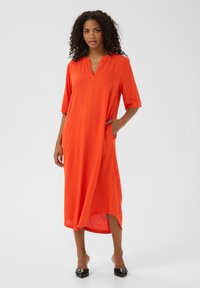 Robe orange, longueur genou, avec un col en V et des manches courtes. Dotée de poches latérales et d'une légère asymétrie au niveau de l'ourlet. Tissu lisse, coupe décontractée.