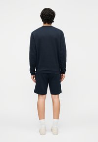 Tumesinise pusa ja lühikeste pükste komplekt. Pusa on ümarkaelusega ja pikkade varrukatega; lühikestel pükstel on elastne vöökoht. Sile, vabaaja kangas.