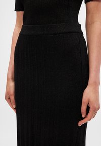 Rochie neagră cu dungi, din fir metalic, având talie ajustată și mâneci scurte. Textură netedă și design care se mulează pe corp.