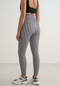 Legginsy w czarno-biały wzór pepitki z wysokim stanem, zestawione z białymi butami sportowymi z czarnymi akcentami.