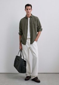 Camisa verde oliva de botones sobre una camiseta blanca, combinada con pantalones de color blanco sucio y zapatos marrón oscuro. Llevando un bolso gris oscuro.