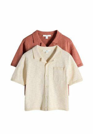 Two short-sleeve knit shirts with collars, one cream button-up with front pocket layered over a rust-colored shirt.
