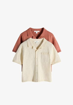 Zwei kurzärmlige Strickshirts mit Kragen, eines cremefarben mit Knopfleiste und Fronttasche, übereinander getragen über einem rostfarbenen Shirt.