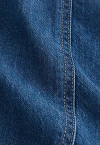 Gros plan sur un tissu en denim bleu avec des coutures oranges détaillées le long d'une couture.