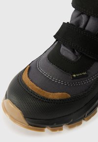 Fekete és szürke vízálló csizma, amely velúr díszítéssel, tépőzáras pántokkal, texturált anyaggal és egy erős gumitalppal rendelkezik, amelynek színe barna.