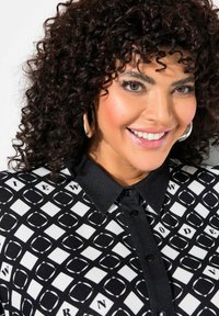 Blusa a stampa bianca e nera con colletto, caratterizzata da forme geometriche e lettere, tessuto testurizzato e bottoni neri.