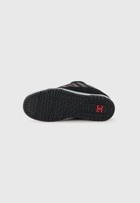Black and gray sneaker sole with a textured tread pattern and a red logo near the heel on a plain white background.