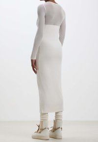 Robe longue ajustée en texture côtelée, couleur blanche, avec des manches longues. Associée à des bottines claires et des jambières côtelées.