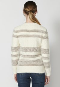 Mõnusalt pehme kuid tekstureeritud fliiskootud sallidega kampsun, millel on horisontaalsed kreemja ja beeži triibud, ümmargune kaelus ja pikad varrukad. Pehme tekstuur on hästi nähtav ja kampsun on veidi laiem.