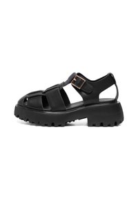 Black sandal with chunky rubber sole, crossed straps, and an adjustable buckle. Features an open heel and textured upper material.