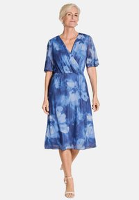 Robe fleurie bleue fluide avec des manches courtes et larges, un décolleté en V et une taille élastique, présentant un tissu léger et transparent.