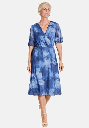 Robe fleurie bleue fluide avec des manches courtes et larges, un décolleté en V et une taille élastique, présentant un tissu léger et transparent.
