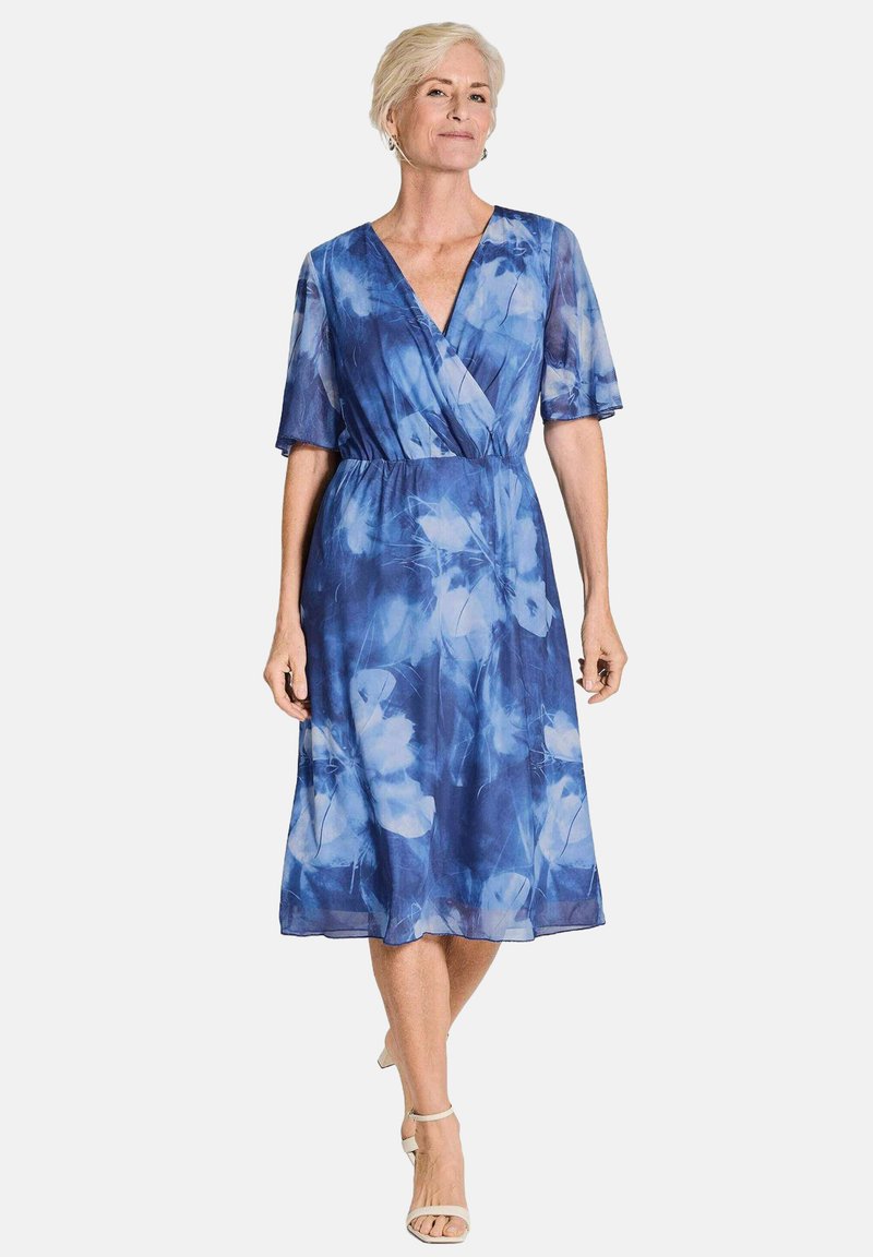 Robe fleurie bleue fluide avec des manches courtes et larges, un décolleté en V et une taille élastique, présentant un tissu léger et transparent.