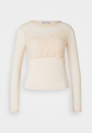T-shirt à manches longues en crème avec un empiècement en dentelle au niveau de la poitrine, présentant un col rond et un tissu lisse pour une silhouette ajustée.