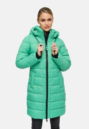 Mujer vestida con un abrigo de invierno acolchado largo en verde menta con capucha, sosteniendo los cordones, de pie contra un fondo blanco liso.
