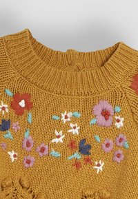 Gelber Strickpullover mit geripptem Kragen, verziert mit bunten floralen Stickereien in Pink, Rot, Blau und Weiß.