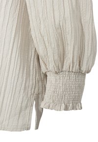 Crèmekleurige blouse met een gestructureerd, geplooid ontwerp; heeft gepofte mouwen met gerimpelde manchetten en een subtiele geruffelde rand.