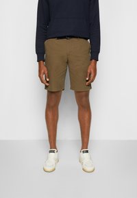 Beige Shorts mit geradem Schnitt, aus Baumwolle. Kombiniert mit einem marineblauen Kapuzenpullover und weißen Sneakers mit Gummisohlen.