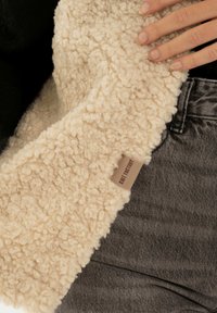 Beige strukturiertes Gewebe mit einer fuzzy Erscheinung, kombiniert mit dunkelgrauem Denim. Verfügt über ein 'Knit Factory'-Etikett am Rand.
