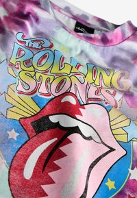 Daudzkrāsains t-krekls ar saistīto krāsu rakstu, kuram ir grafika ar muti sarkanā un rozā krāsā ar melnu kontūru un teksts "The Rolling Stones" dzeltenā krāsā.