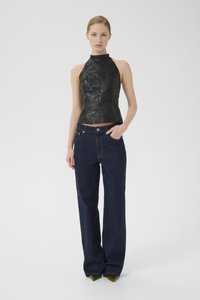 Svart lær halterneck-topp med teksturert overflate og en tett passform, sammen med mørkeblå vide jeans med en svak glans.