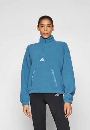 Blauer Fleece-Pullover mit halber Reißverschluss-Kragen, ausgestattet mit zwei vertikalen Taschen mit blauen Akzenten und einem kleinen Logo auf der Brust.
