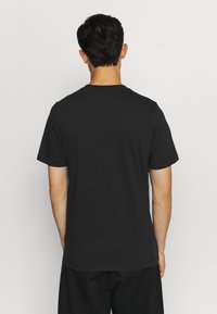 Svart bomullströja med rund hals och korta ärmar, som visar en jämn textur och enkel design från baksidan.