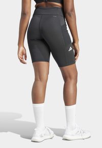 Pantalones cortos deportivos negros con una cintura alta, que presentan un acento de logo. Combinados con calcetas blancas hasta la rodilla y zapatillas de deporte blancas.