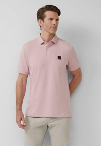 Polo rose clair en mélange de coton, avec un col classique, trois boutons, et un patch logo noir sur le côté gauche de la poitrine.