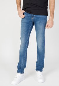 Vaqueros de mezclilla azul claro con corte recto, aspecto desgastado y diseño clásico de cinco bolsillos. Combinados con zapatillas blancas.