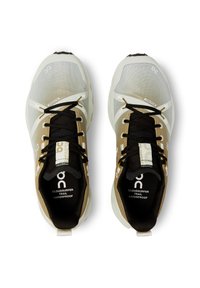 Un paio di scarpe da trail running impermeabili beige, bianche e nere con lacci neri viste dall'alto su sfondo bianco.