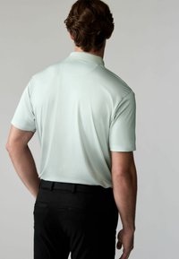 Mintgrünes Poloshirt mit kurzen Ärmeln, einem kragenlosen Ausschnitt und strukturiertem Stoff, kombiniert mit schwarzen Hosen, von hinten betrachtet.