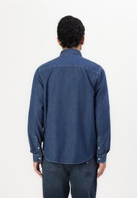 Donkerblauw denim overhemd met een button-down kraag, lange mouwen en een gebogen zoom. Voorzien van dubbele knopenmanchetten en een soepele textuur.