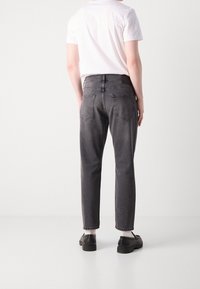 Mörkgrå jeans med rak benpassform, utrustad med två bakfickor och dragkedja. Bärs med en vit T-shirt och svarta skor.