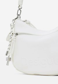 Weißes Handtasche mit geschwungener Form, glattem Material, Reißverschlussverschluss, geknoteten Stoffakzenten und silbernen Hardware-Details.