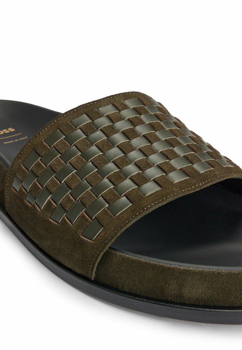 Sandały z przesuwanym noskiem, wykonane z ciemnozielonego zamszu oraz plecionki skórzanej, czarne wnętrze i czarna podeszwa, ujęcie z bliska na białym tle.