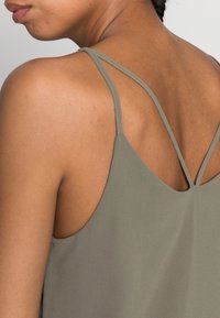 Top senza maniche verde oliva con design a V sulla schiena. Caratterizzato da spalline sottili e texture liscia, mette in evidenza il collo della schiena.