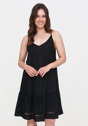 Czarna sukienka bez rękawów z dekoltem w kształcie litery V, z dopasowanym topem i rozkloszowanym, piętrowym dołem z poziomymi wycięciami. Gładka faktura materiału.