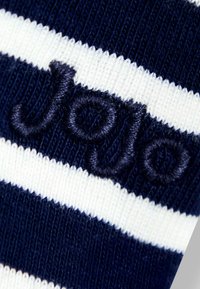 Temno plava čarapa sa prugama bijele boje; sadrži izvezeni tekst "Jojo" u tamnoplavoj niti, od teksturiranog pletenog materijala.