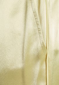 Satintyg i blekgul, med en slät textur och subtil lyster. Inkluderar en sömdetalj och en gömd ficka på sidan.