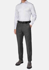 Man som bär en ljusgrå knappad skjorta instoppad i mörkgrå byxor, svart flätad bälte och grå mocka Chelsea-boots.