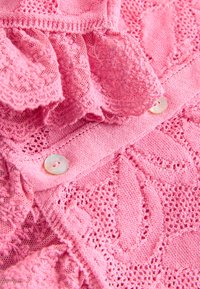 Rosa Strickstoff mit Spitzenverzierungen, strukturierten Mustern und einem Zwei-Knopf-Verschluss mit Perlmuttknöpfen.